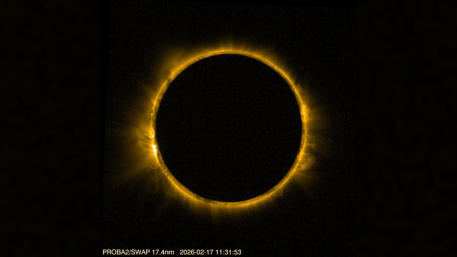 detailed view of the sun blocked by the moon in the center, creating a dramatic ring of fire against a black background. The sun's corona is visible around the edge of the moon. 
