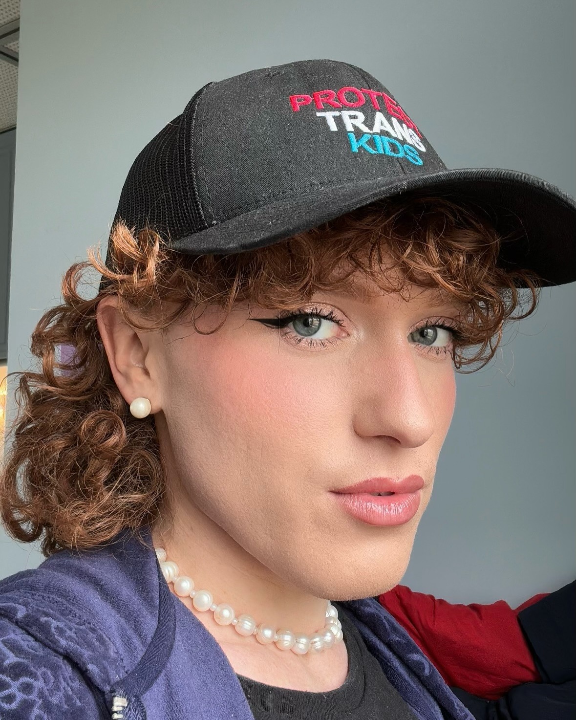 A selfie of Eli Levi wearing a Protect Trans Kids hat.