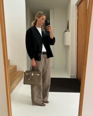 @anoukyve wearing a black jacket with a white T-shirt, brown jeans, and a brown Hermès Birkin bag.