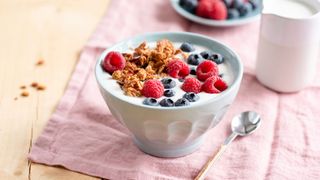 Bowl of cereal and milk with berries on top.