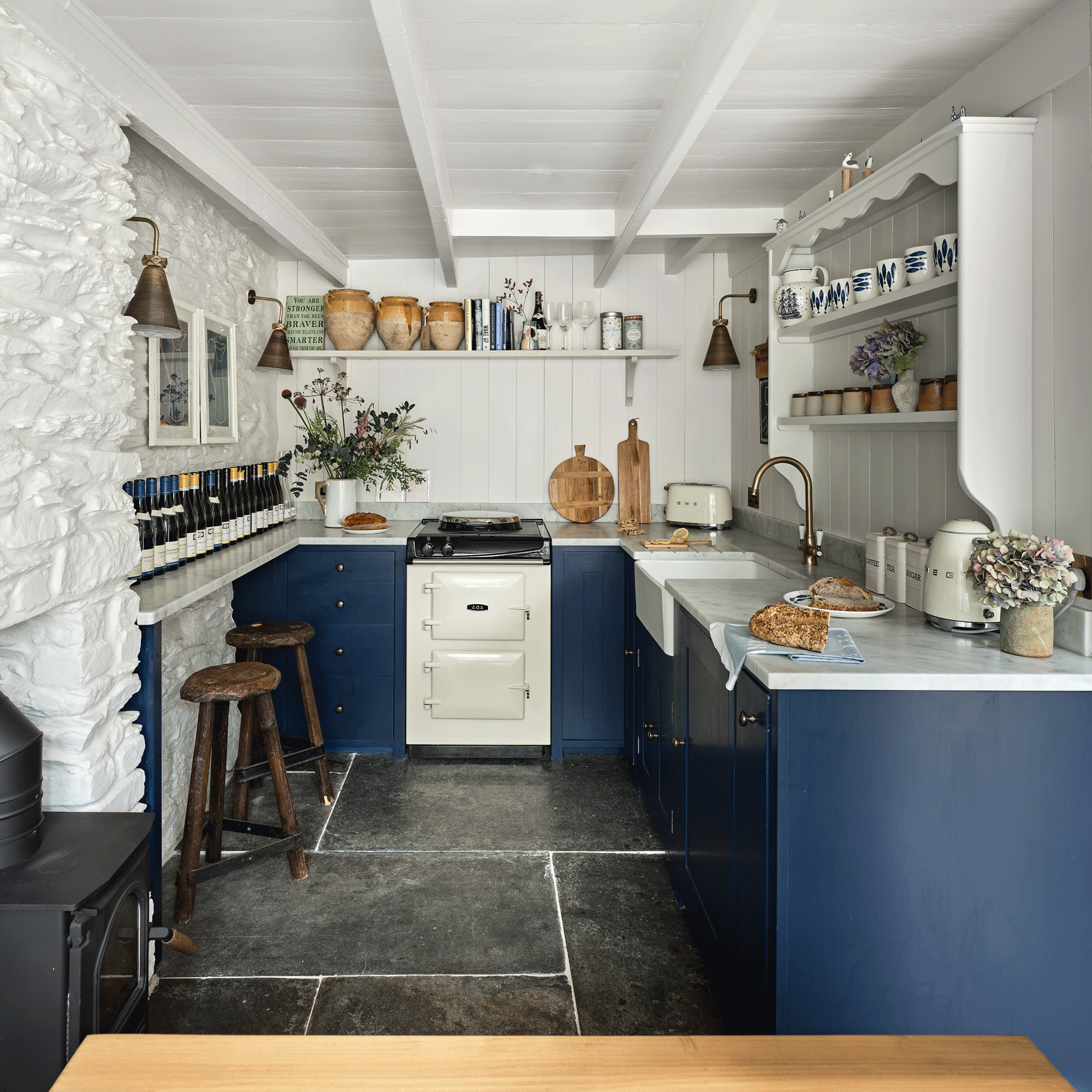 a compact blue and white kitchen with blue cabinetry and white walls and open shelving and a matching small white range cooker
