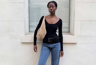 Sylvie Mus wears a black long-sleeve top, blue jeans, black belt, black mules, and a beige suede bag.