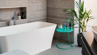 Neutral tiled walls in bathroom with freestanding bath and side table with houseplant