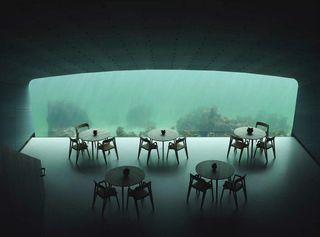 An interior of an underwater restaurant, the table and chairs face a glass wall looking out into the seabed