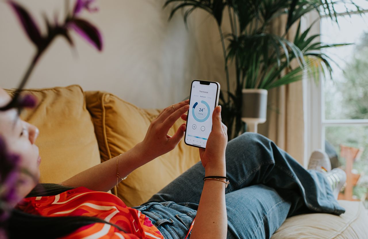 A woman relaxing on the sofa using a thermostat app on her smart phone.