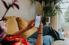 A woman relaxing on the sofa using a thermostat app on her smart phone.