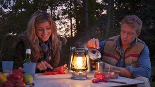 best camping lantern: camping couple at a table lit by lantern