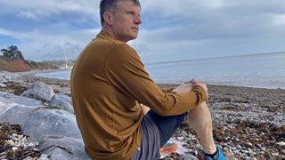 A man wearing a Smartwool Men's Classic All-Season Merino Base Layer Long Sleeve sitting on a stony beach.
