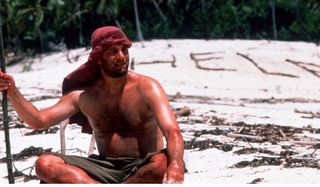 Cast Away Tom Hanks sits on a beach, with a stick