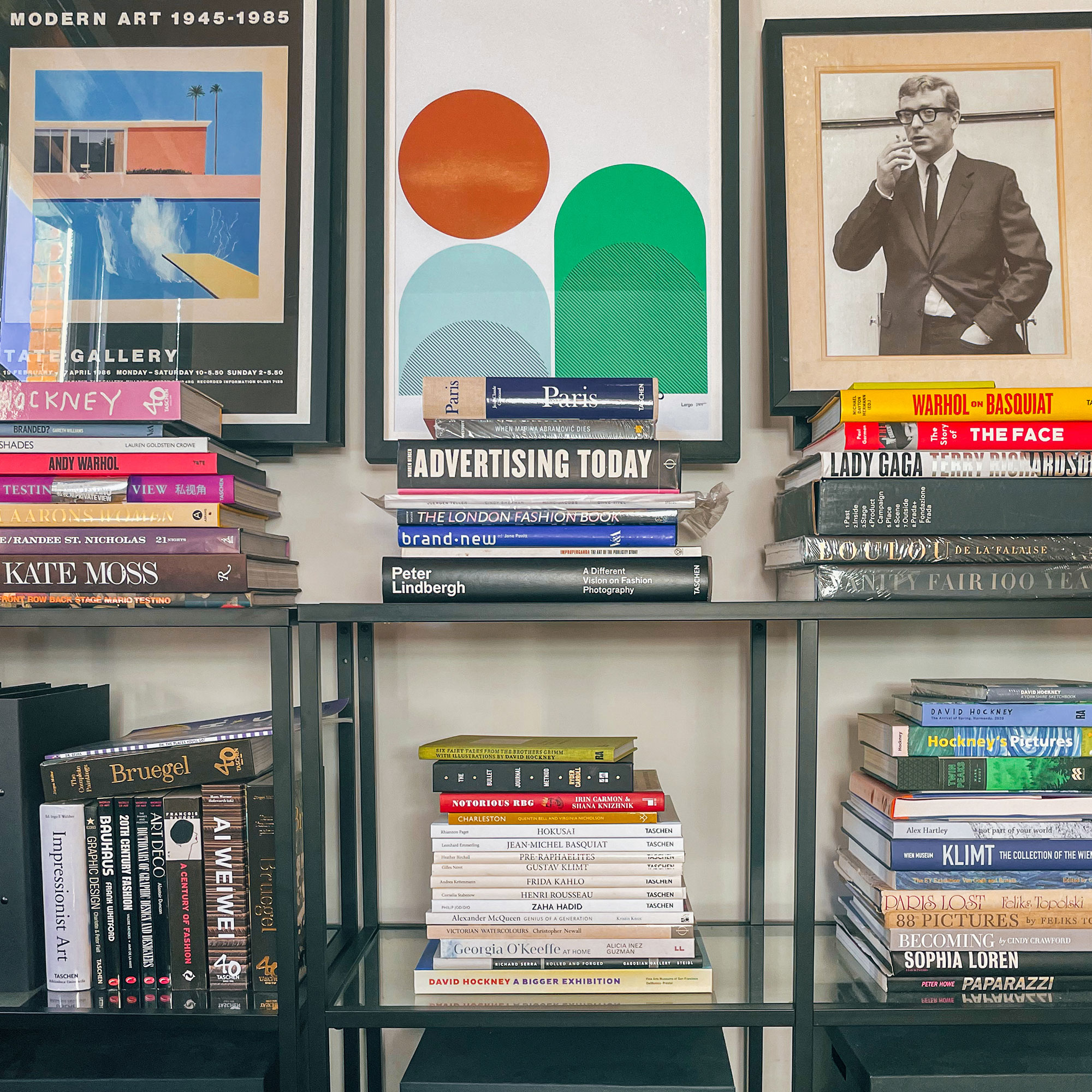 Black bookshelves with stacks of books, topped with art prints