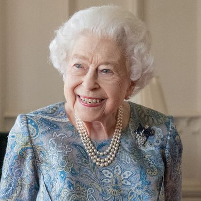 Queen Elizabeth II smiles and has white hair, is wearing a white pearl necklace, and a blue and turquoise brocade dress, Sarah Ferguson wears a smart cream jacket and a wide-brimmed black hat