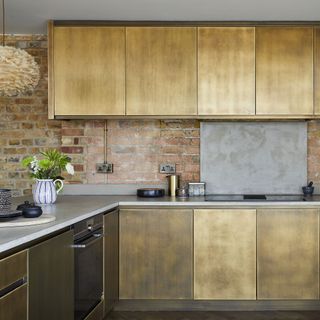 Gold kitchen cabinets, brick wall, and silver worktops
