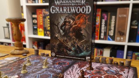 A wide shot of the Warhammer Underworlds: Gnarlwood box with the board and pieces on a wooden table