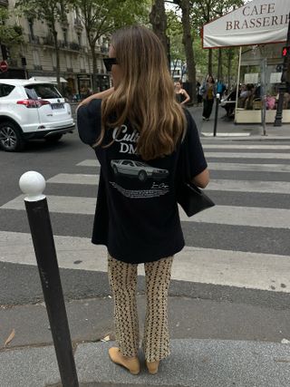 Woman walks down a street in Paris in a vintage black t-shirt, patterned pants, and ballet flats.