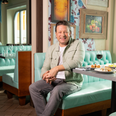 jamie oliver on banquette seat in restaurant in front of paintings and patterned wall paper