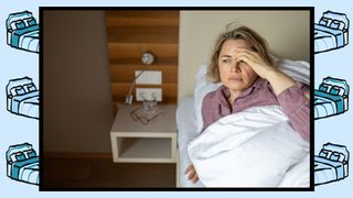 A menopausal woman with blonde hair sitting up in bed with hand over forehead