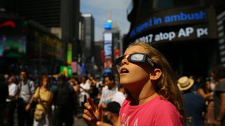 A girl observes the total solar eclipse with solar eclipse glasses at Times Square in New York City, United States on August 21, 2017.