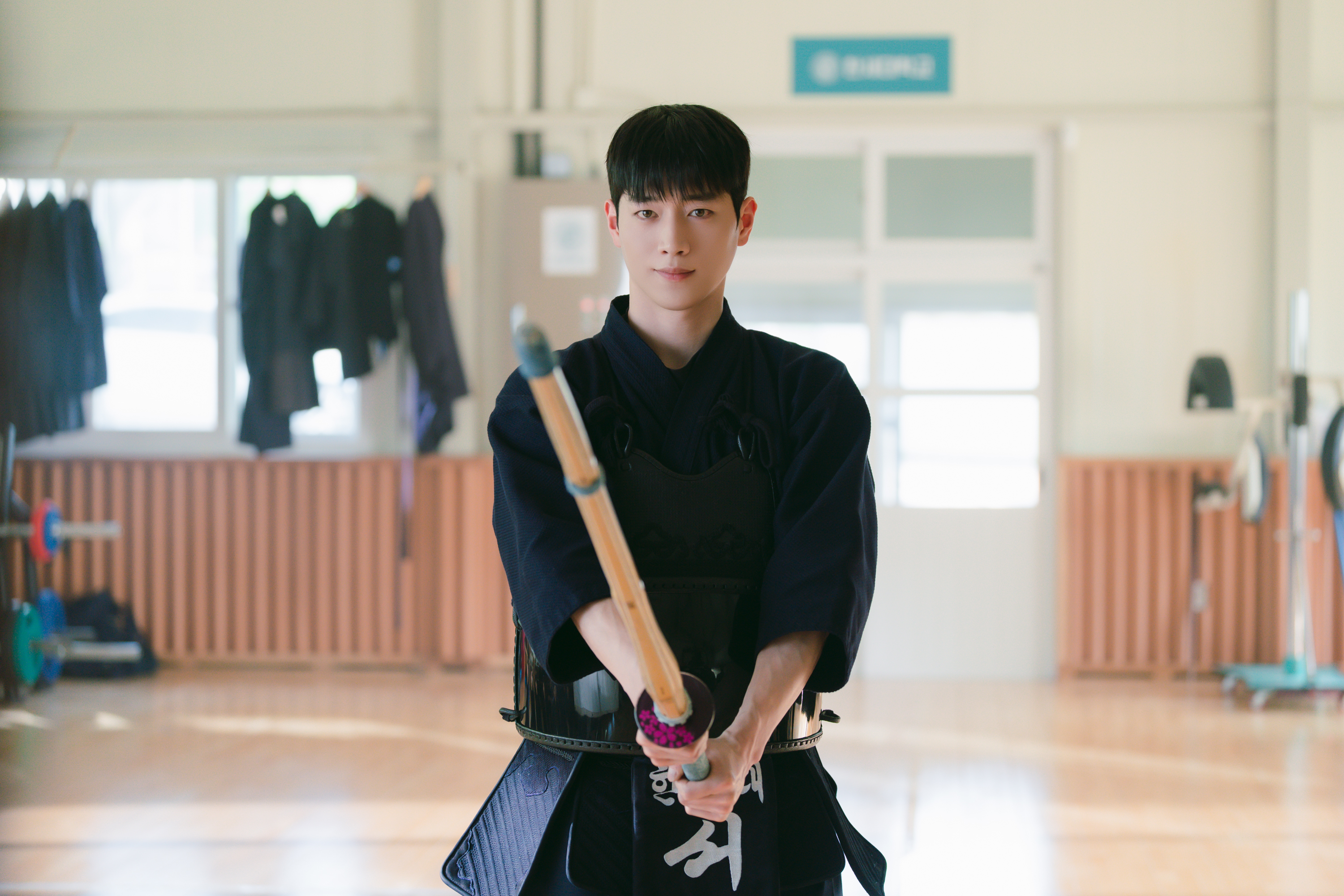 A man (Seo Kang-jun as Seo Eun-ho) wears an all-black kumdo uniform and holds a kumdo sword, while standing in a martial-arts studio, in the Netflix K-drama 'Boyfriend on Demand.'