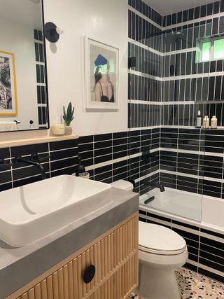 Black tile shower enclosure with white tub and terrazzo floor