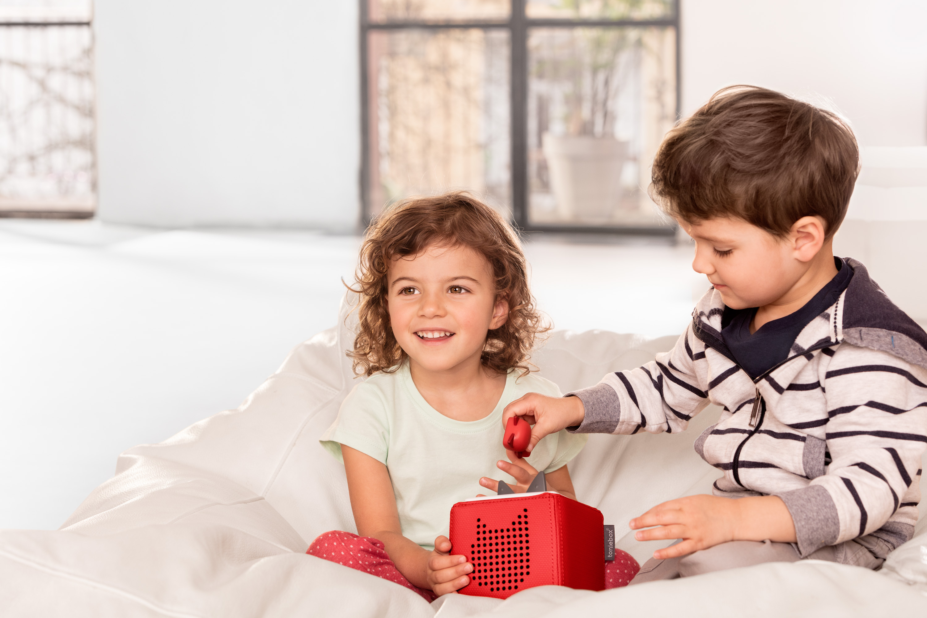 Two kids at home playing with a red Toniebox and creative Tonie figure