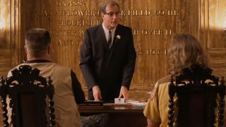 Warren Keith in a suit standing in front of John Goodman and Jeff Bridges in The Big Lebowski