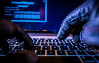 A hacker wearing black gloves using a laptop keyboard