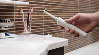 A close-up picture of a man holding an electric toothbrush near the bathroom sink