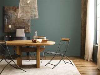 A dining room painting in an earthy dark green colour with a wooden and metal dining set