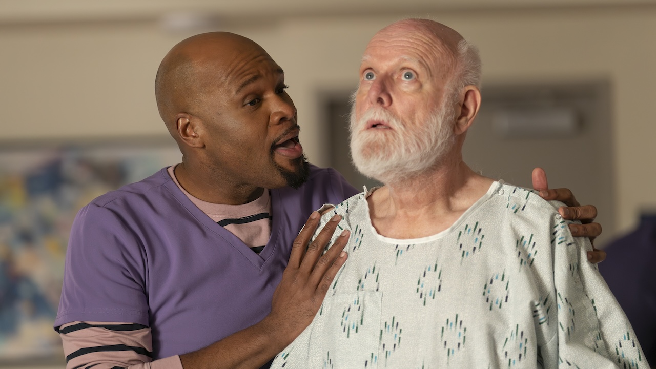 Nurse DuBois handling an older patient in the Sacred Heart lobby on Scrubs