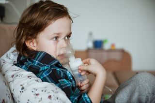 A preschool-age child using a nebulizer while relaxing on the couch.