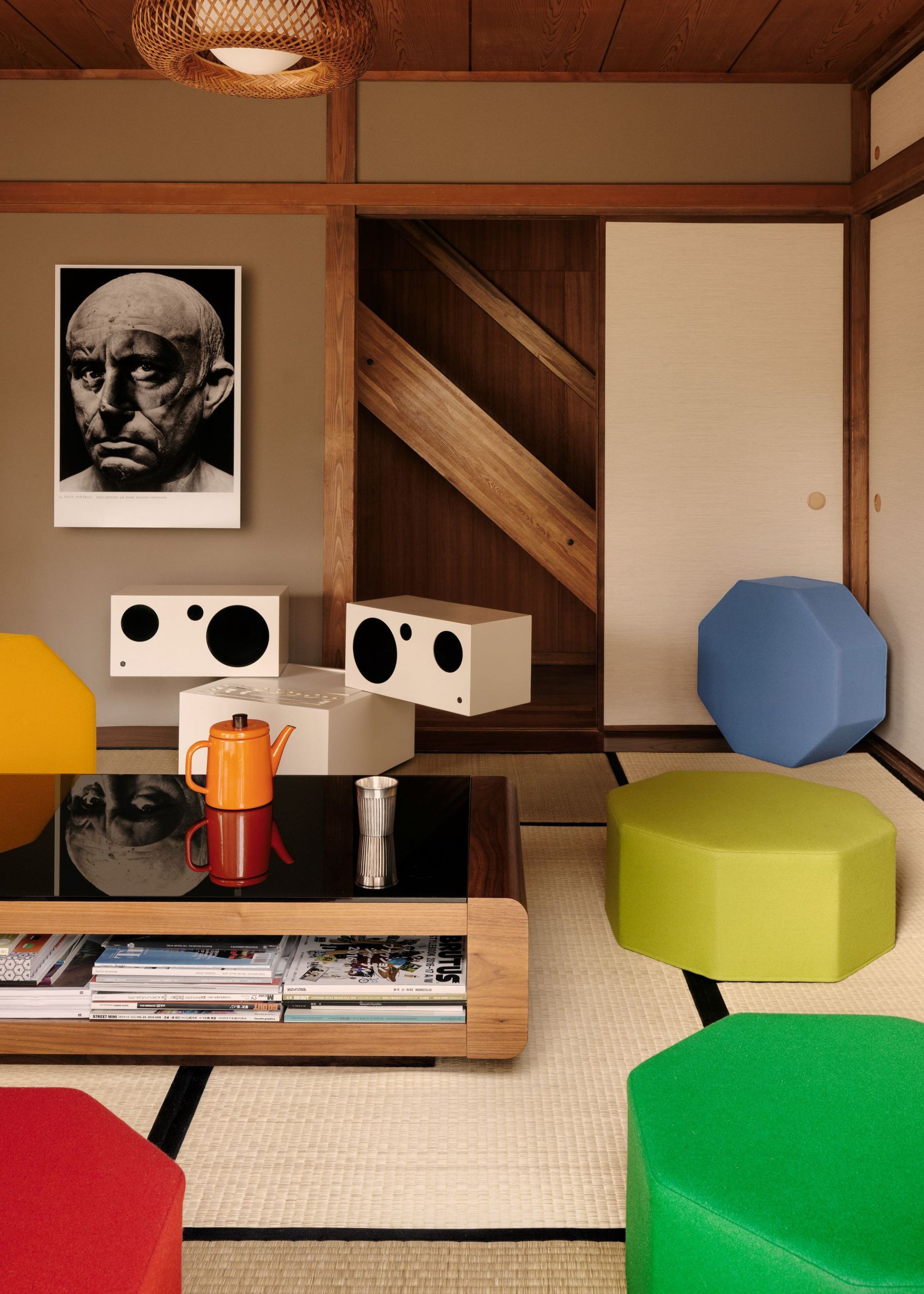 An abstract and colorful Japanese living room with angular yet inviting colorful stools and seating around a low profile coffee table with too cups on top and white futuristic style speakers