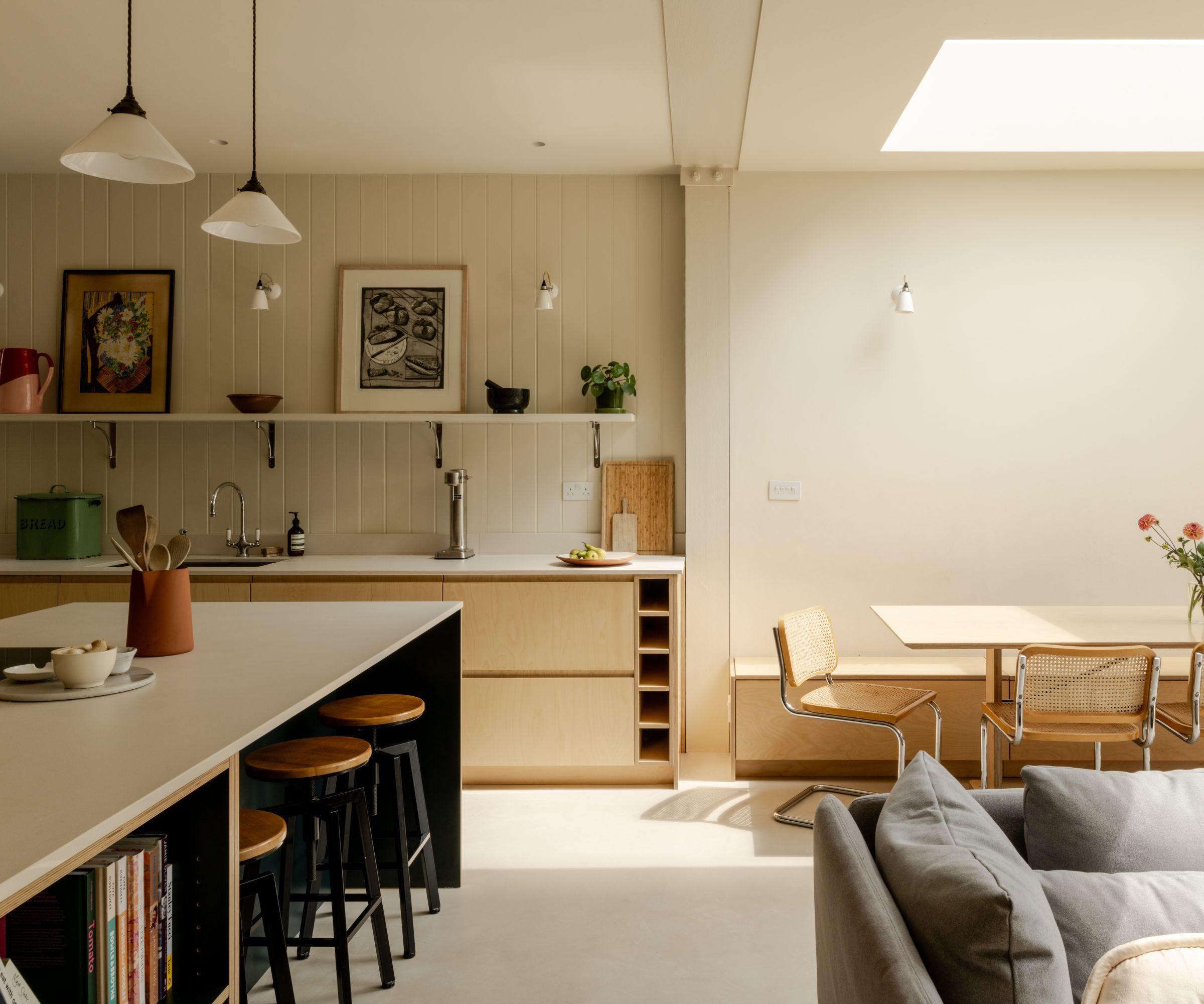 Bright, airy open-concept kitchen and dining area with pale wood lower cabinets, cream walls, and a large skylight pouring natural light.
