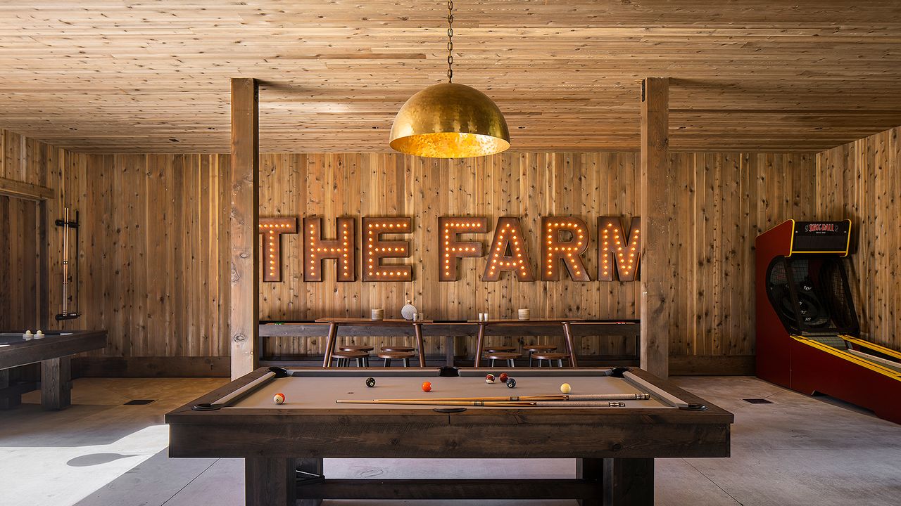 Barn space games room with large brass dome pendant, wood paneling on walls and ceiling, and &#039;the farm&#039; wall decor light sign.