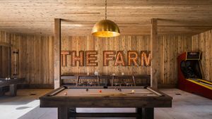 Barn space games room with large brass dome pendant, wood paneling on walls and ceiling, and 'the farm' wall decor light sign.