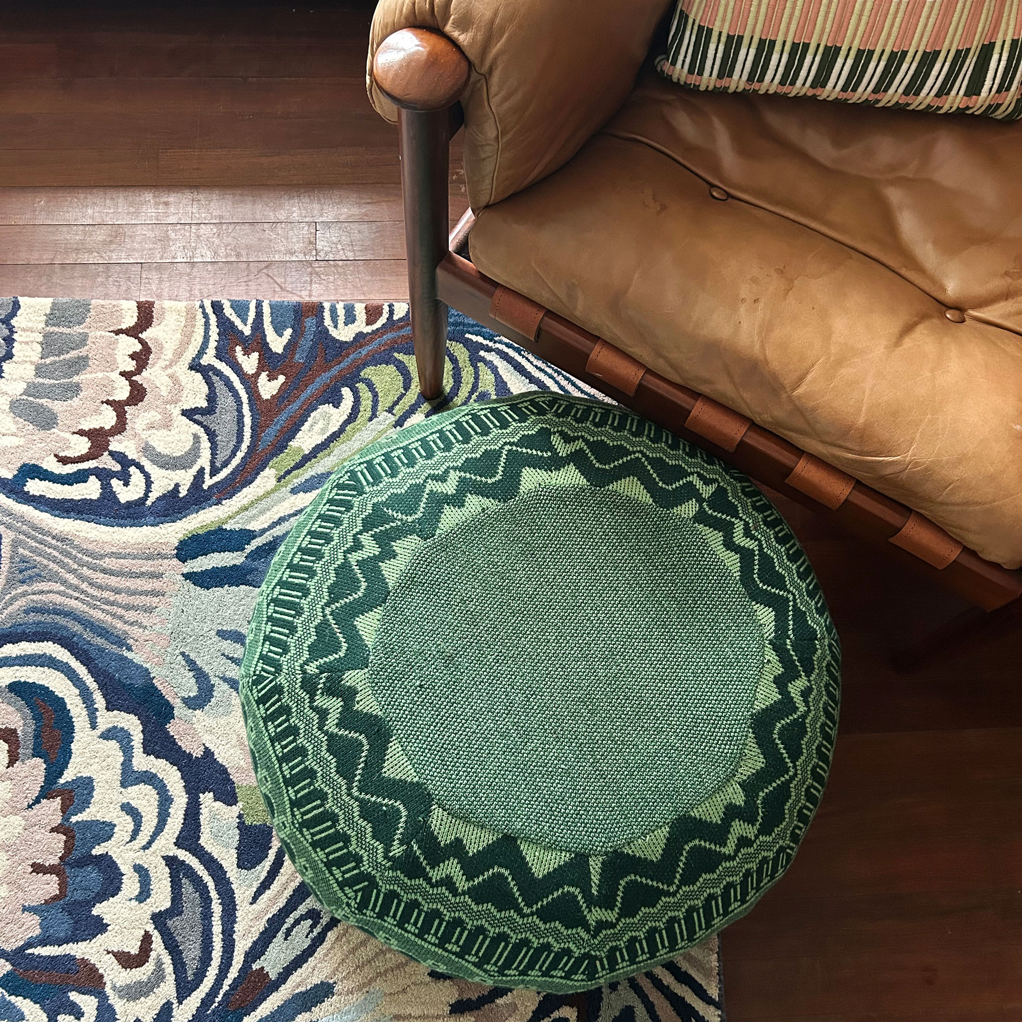 Brown leather armchair with green patterned pouffe and blue marbled rug