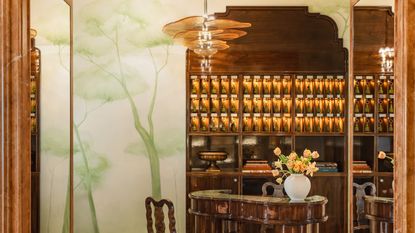 A whimsically decorated hotel lobby, with lacquered wooden cabinetry, a murano glass, flower-like chandelier, and handprinted tree murals in soft tones of green.