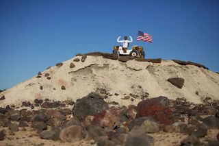 NASA's Robonaut 2, or R2, humanoid robot poses like a champion with the American flag while sitting atop a hill and riding its new wheeled base, Centaur 2, at the Johnson Space Center Planetary Analog Test Site in Houston.