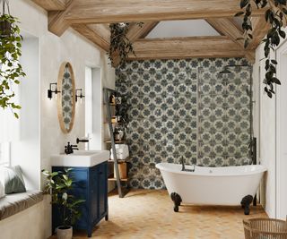 cottage bathroom with rear tiled wall, glass shower screen in front of walk in shower, roll top bath, exposed beams, tiled floor and bue vanity unit with white sink