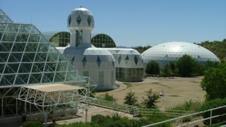 A series of glass domes stand next to other glass buildings on an arid compound with the hot desert sun beating down