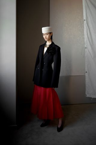 A model wearing a black blazer, red skirt, and white pillbox skirt at the Altuzarra S/S 25 runway show.