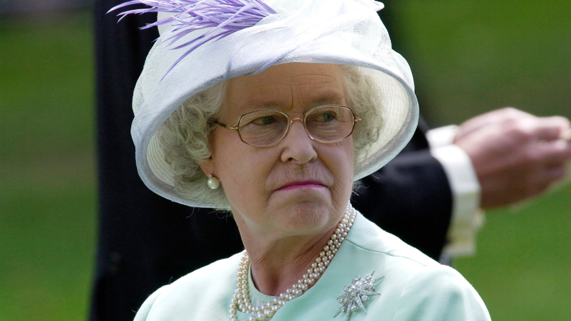 Queen Elizabeth wears a mint green suit and matching hat with a brooch and pearl necklace
