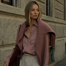 Anouk wears a pink sweater, pink satin button down shirt and beige trousers.