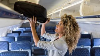 Best carry-on luggage: Image shows a smiling woman lifting a backpack into the overhead compartment of a plane.