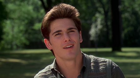 Michael Schoeffling with a sly smile in front of a park at the end of Sixteen Candles. 