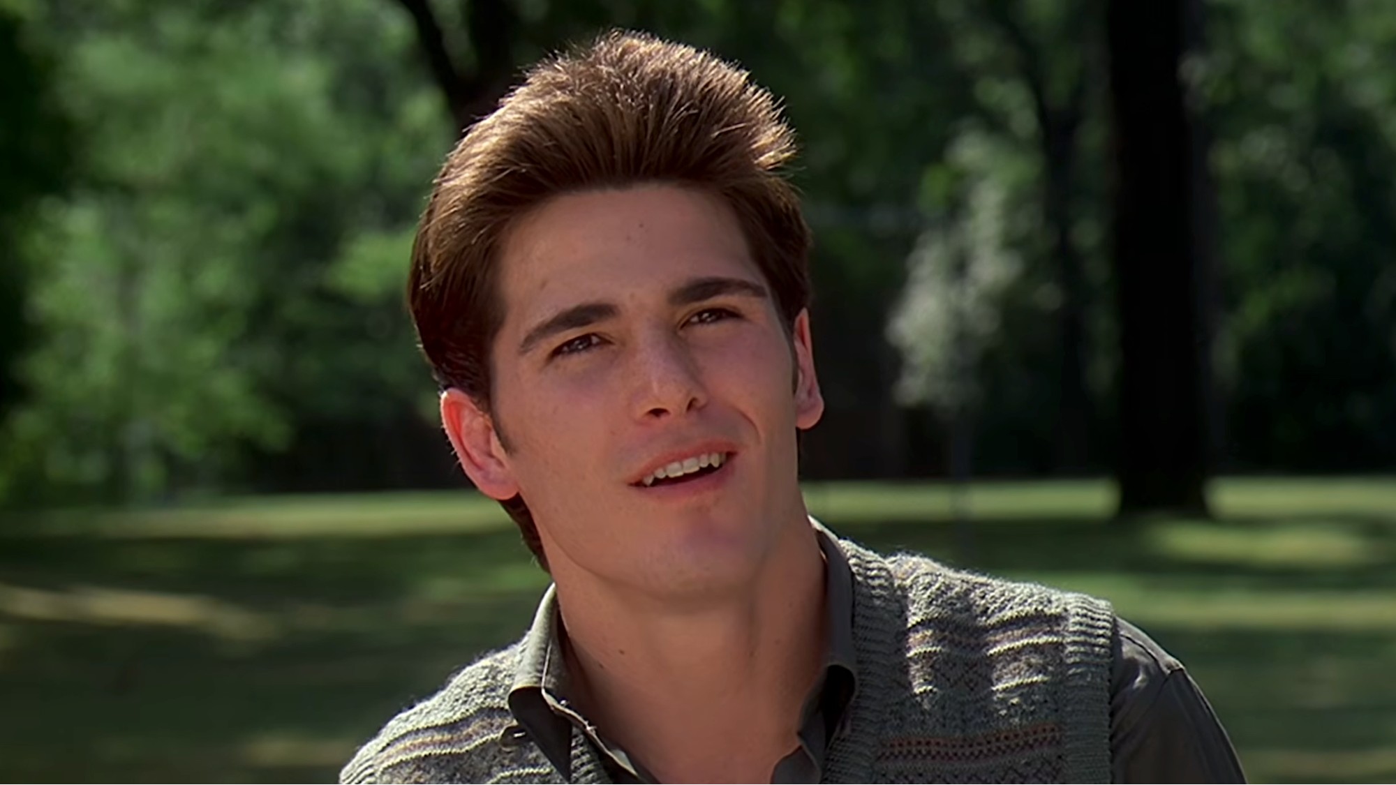 Michael Schoeffling with a sly smile in front of a park at the end of Sixteen Candles. 