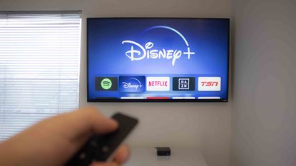 A person in a plain apartment looks for streaming channels, including Disney+