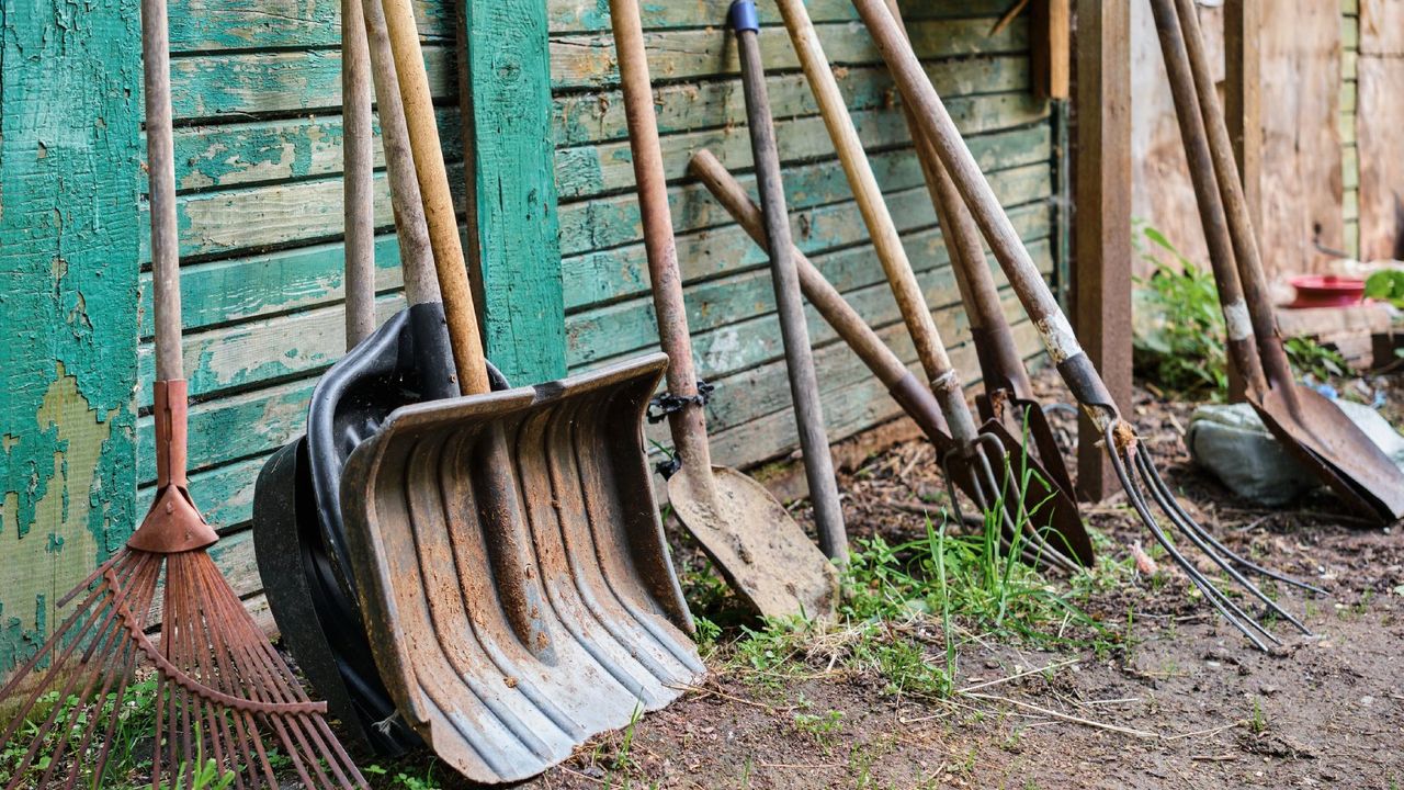 A row of garden tools leaning against a wall with peeling paint