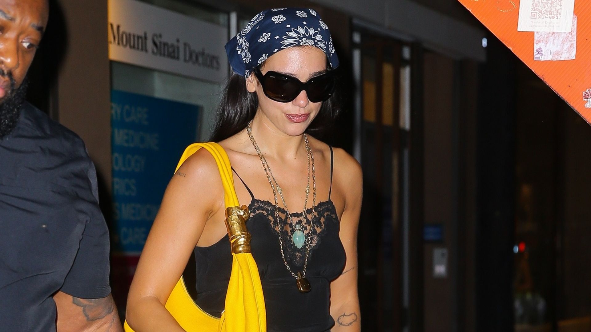 Dua Lipa wears a black cotton dress with black knee-high boots.