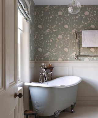 A traditional bathroom with green floral wallpaper, white wall paneling and small pale blue bathtub