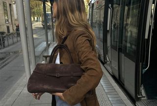 Woman wearing a brown suede coat and holding a chocolate brown suede handbag.